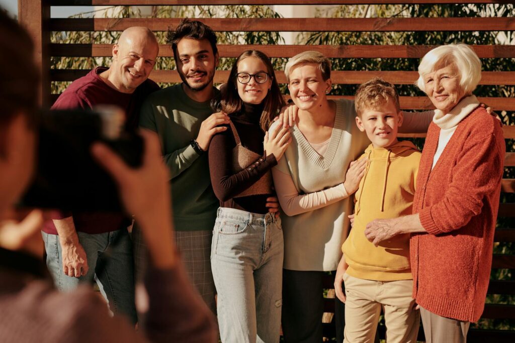 A joyful family portrait featuring multiple generations smiling outdoors in daylight.