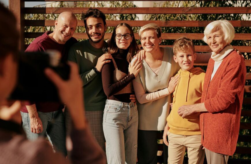 A joyful family portrait featuring multiple generations smiling outdoors in daylight.