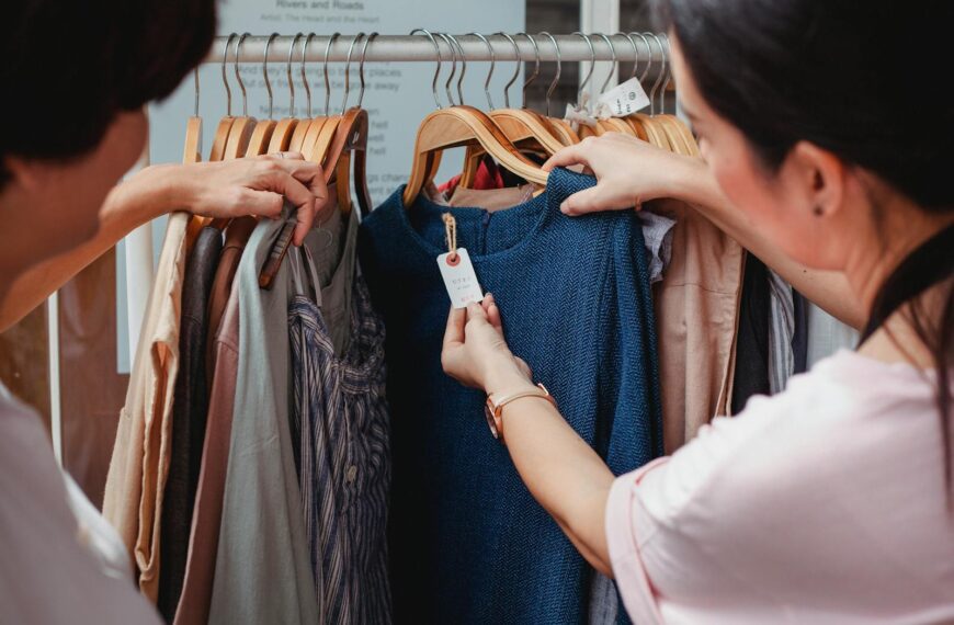 Two women browse clothes in a boutique, examining a blue dress.