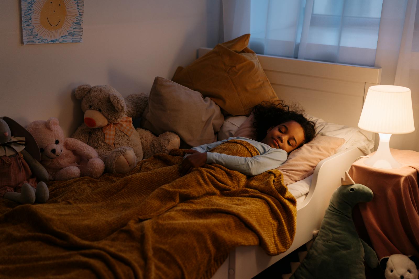 Peaceful young girl sleeping in bed surrounded by stuffed toys and warm lighting.