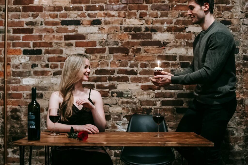 A young couple enjoying a romantic dinner indoors with wine and a cupcake to celebrate a special occasion.