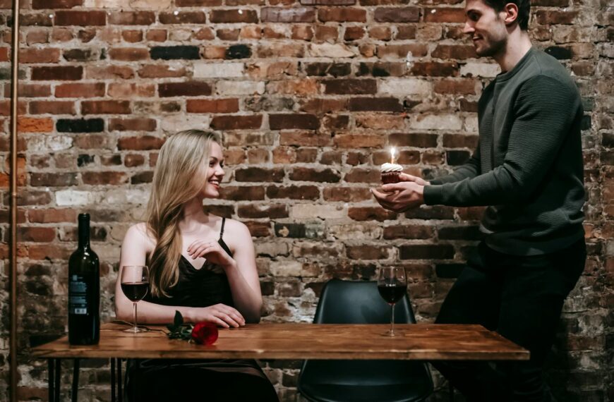 A young couple enjoying a romantic dinner indoors with wine and a cupcake to celebrate a special occasion.