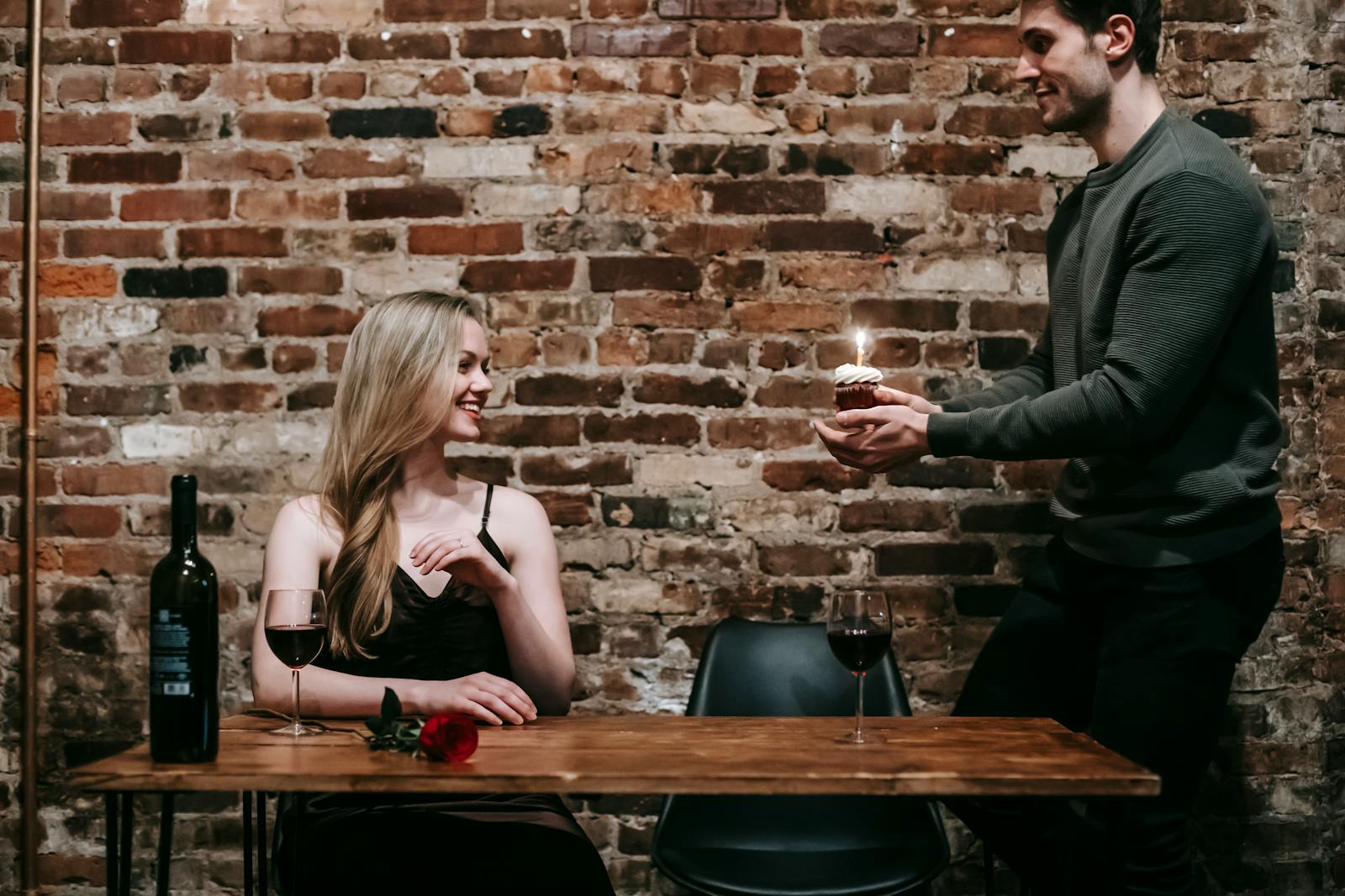 A young couple enjoying a romantic dinner indoors with wine and a cupcake to celebrate a special occasion.