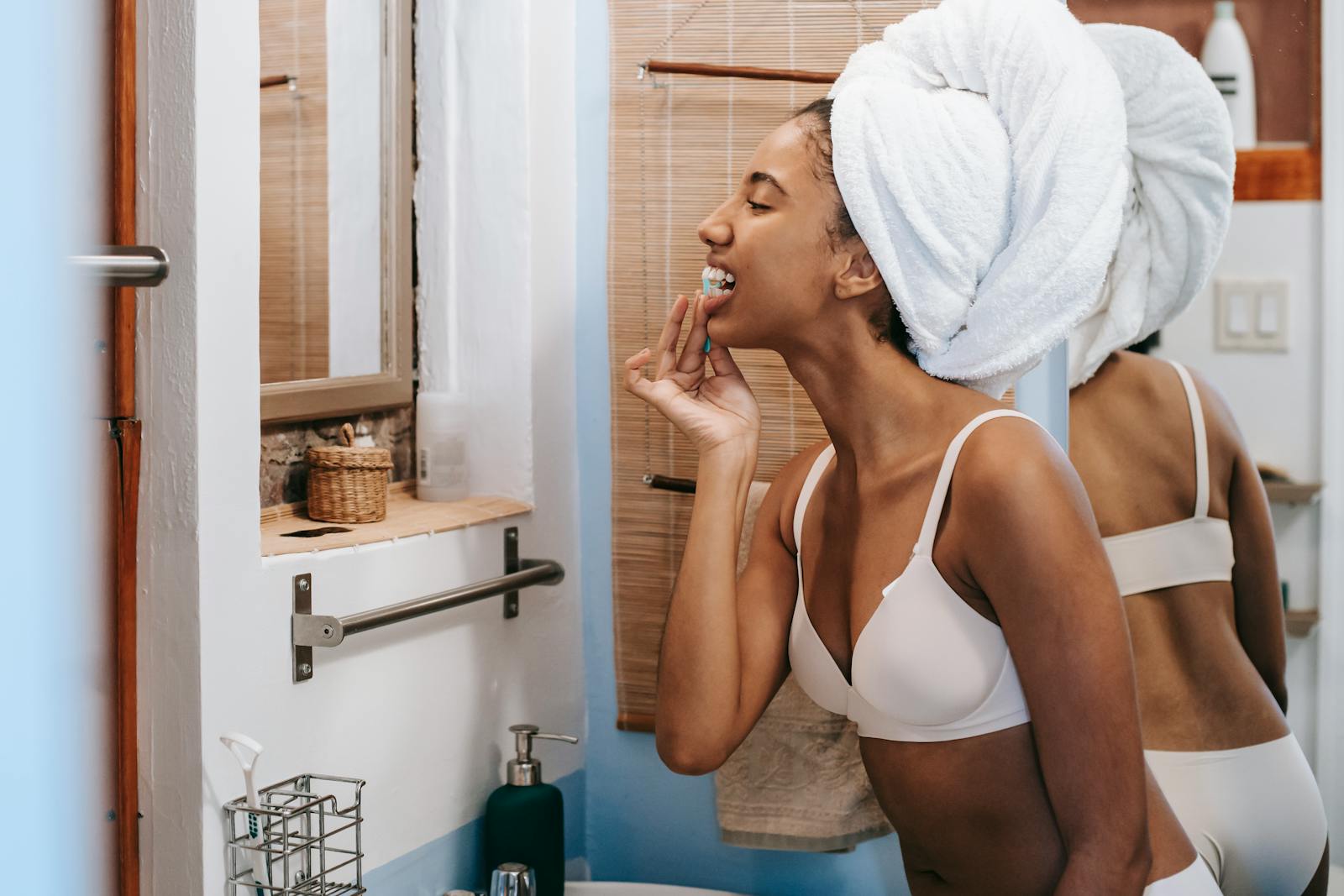 A young woman in a bathroom flossing her teeth with a towel wrapped around her head, promoting oral hygiene.