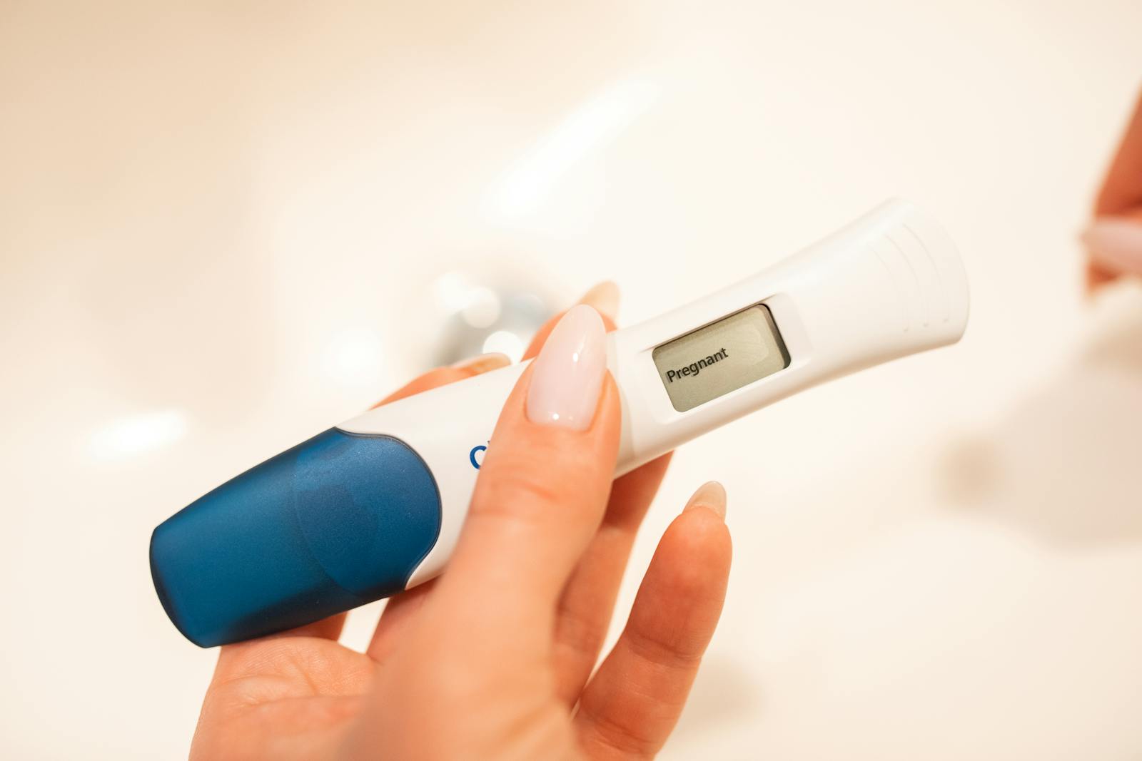 Close-up view of a positive digital pregnancy test held by a woman with manicured nails.