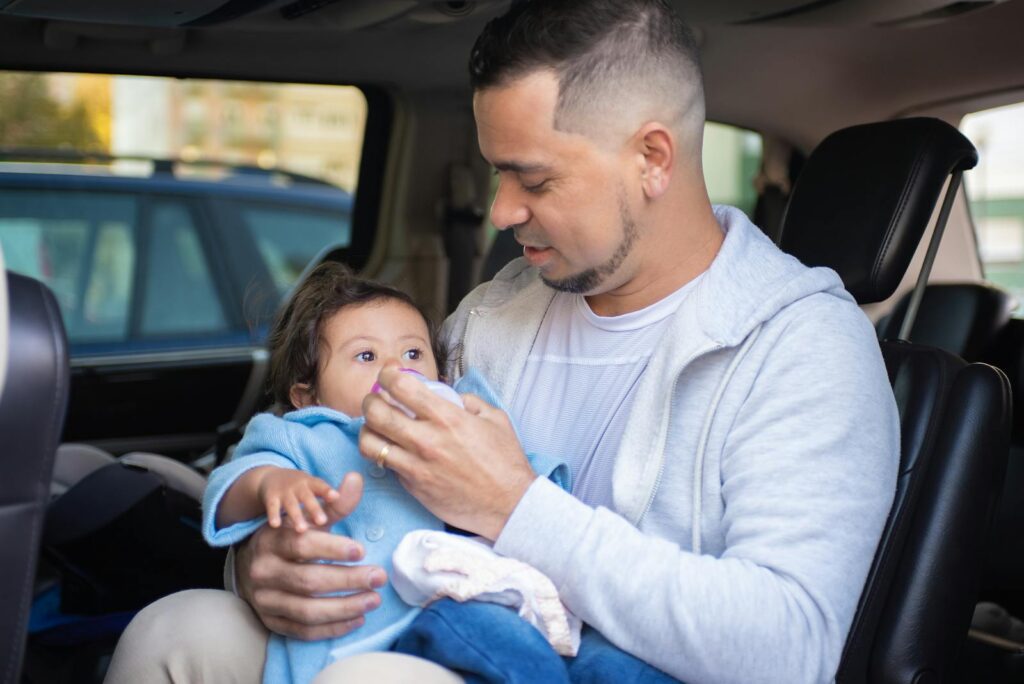 Caring father feeding baby with a bottle inside a car, expressing warmth and connection.