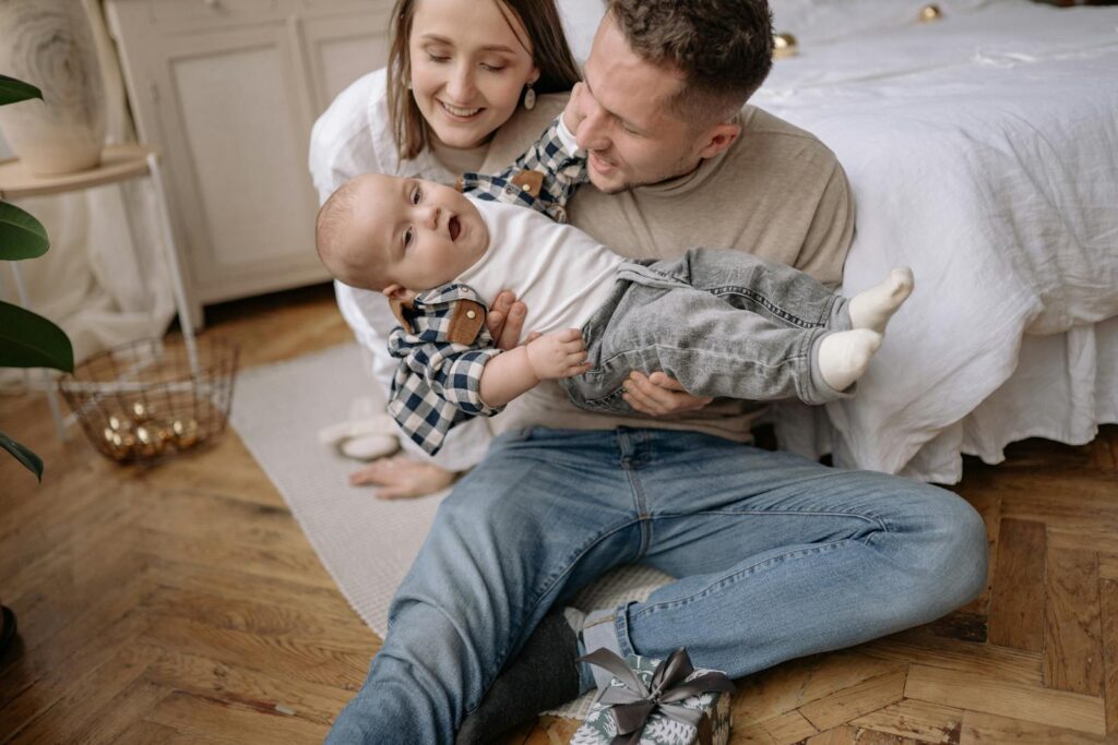 Loving parents sitting with their cheerful baby in a cozy indoor setting, sharing joyful moments.