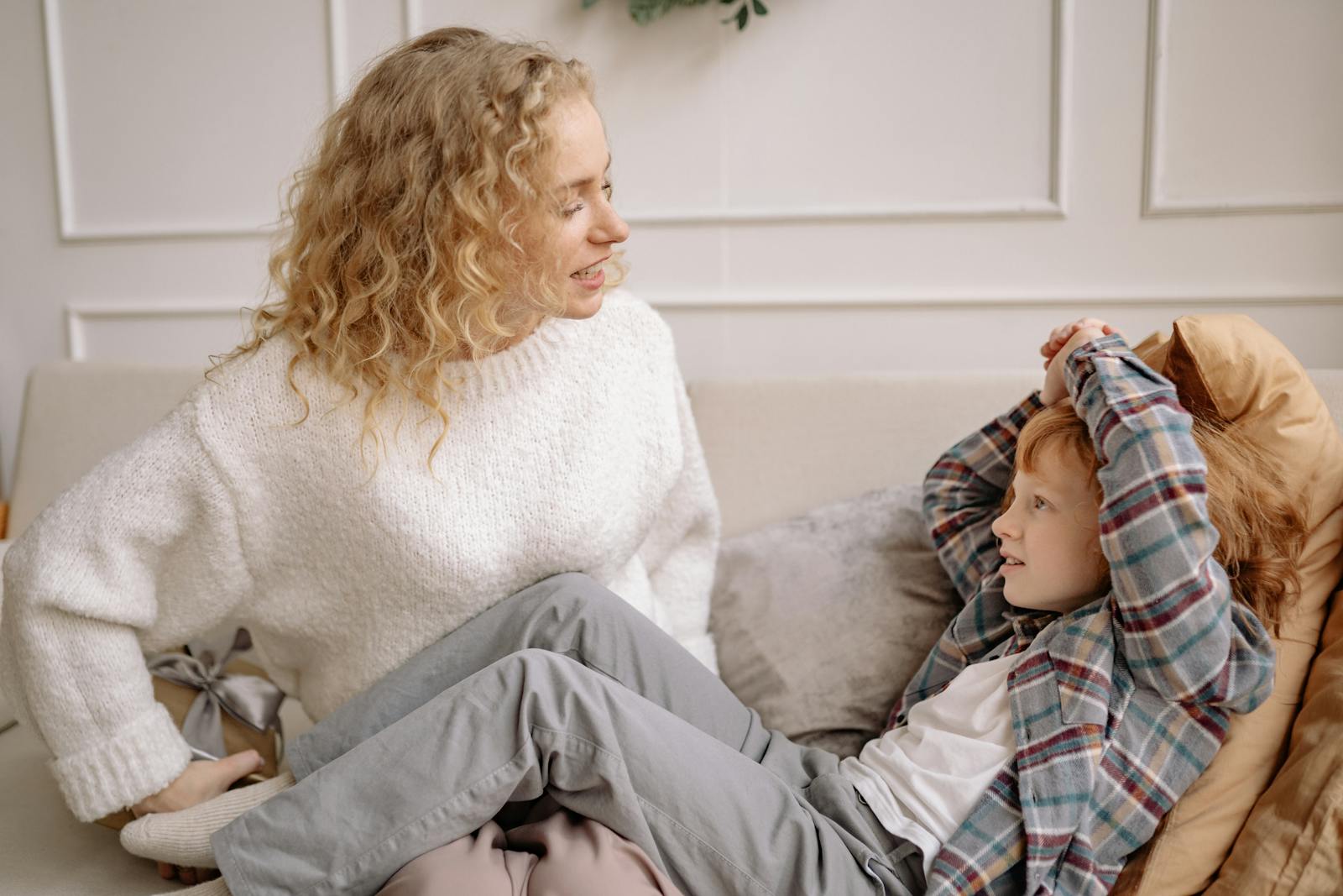 A joyful mother and son smiling at each other while sitting on a couch indoors, creating a warm family moment.