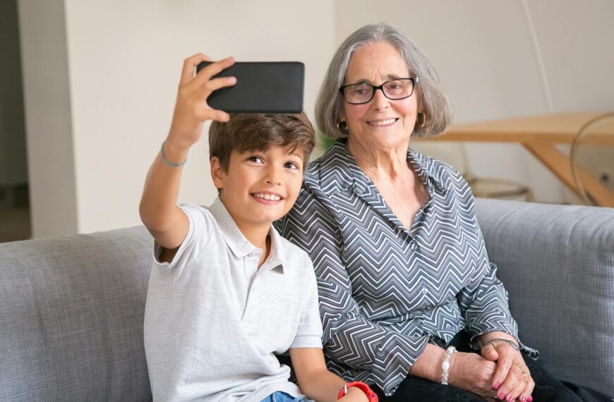Happy grandmother and grandson enjoying a selfie moment on the couch indoors.