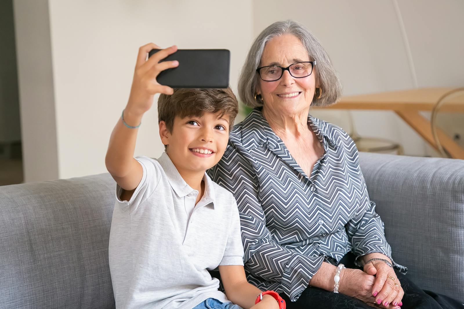 Happy grandmother and grandson enjoying a selfie moment on the couch indoors.