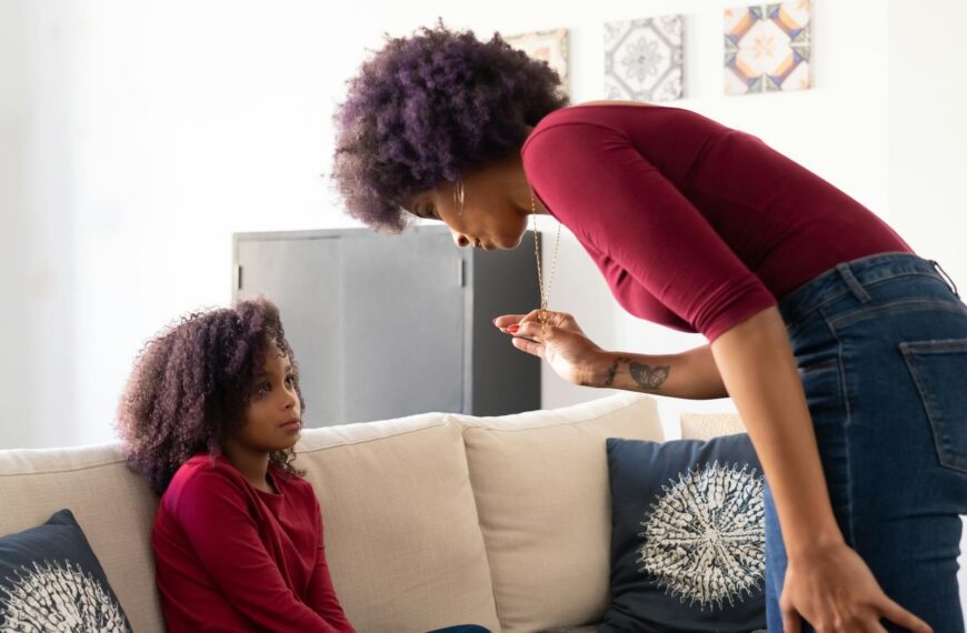 A mother and daughter with afro hair sit on a couch having a serious conversation at home.