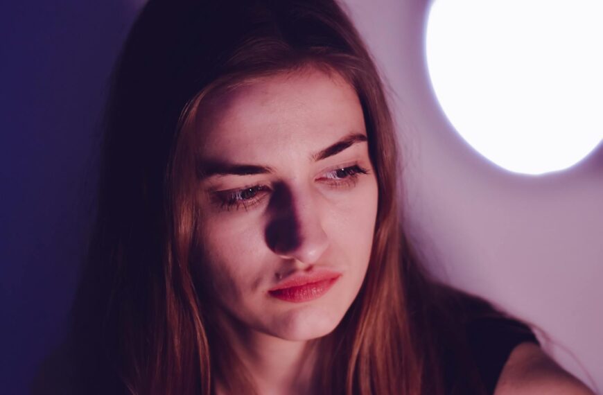 A young woman with long hair gazes thoughtfully, illuminated by gentle lighting indoors.