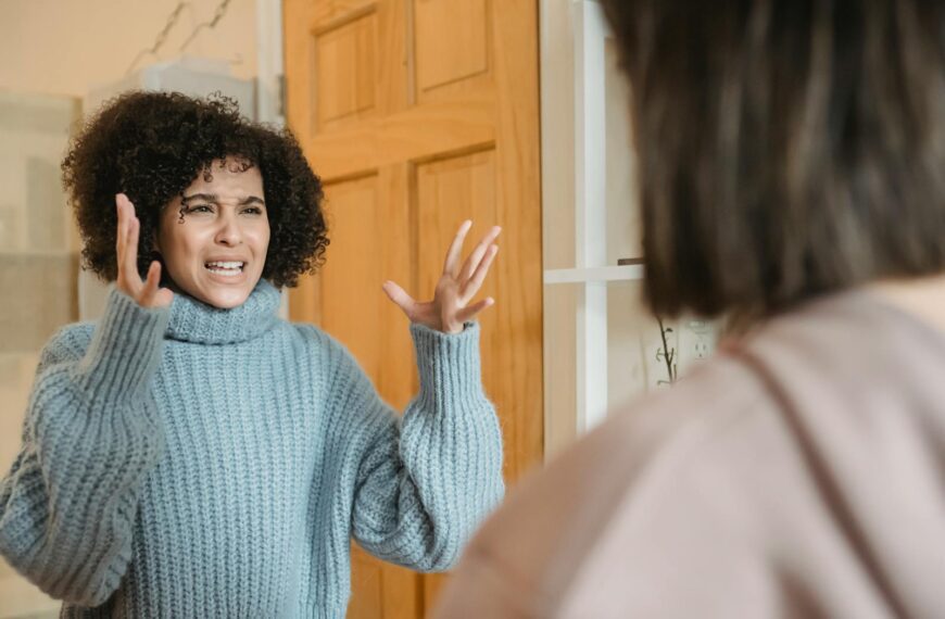 Angry young multiracial ladies in casual clothes standing in bright apartment near door while having disagreement and looking at each other