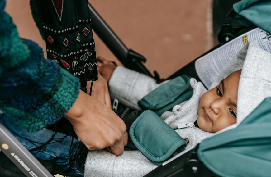 Parent securing baby in stroller outdoors with detailed cloth pattern, expressing care and tenderness.