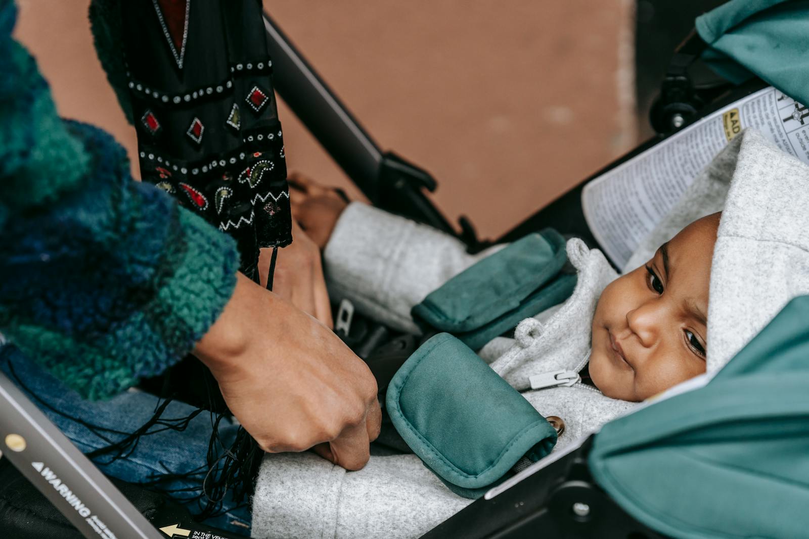 Parent securing baby in stroller outdoors with detailed cloth pattern, expressing care and tenderness.