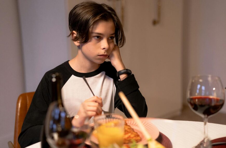Teenage boy sitting at a dining table, appearing thoughtful during dinner indoors.