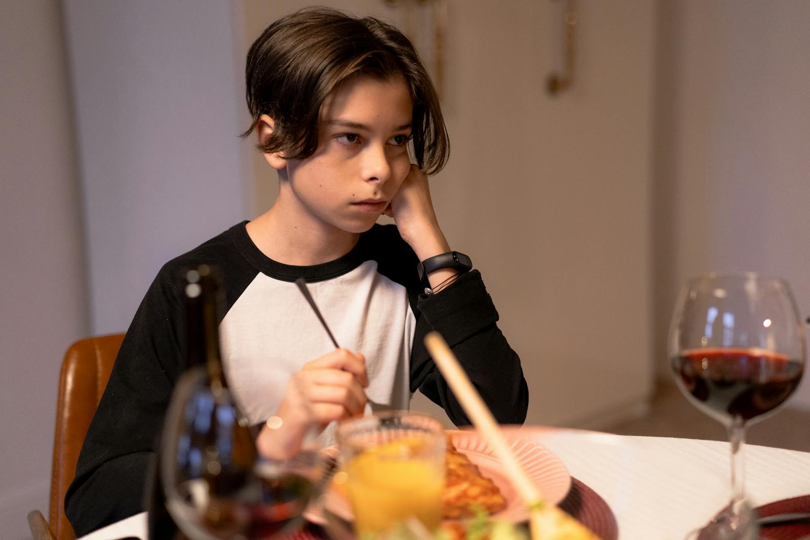 Teenage boy sitting at a dining table, appearing thoughtful during dinner indoors.