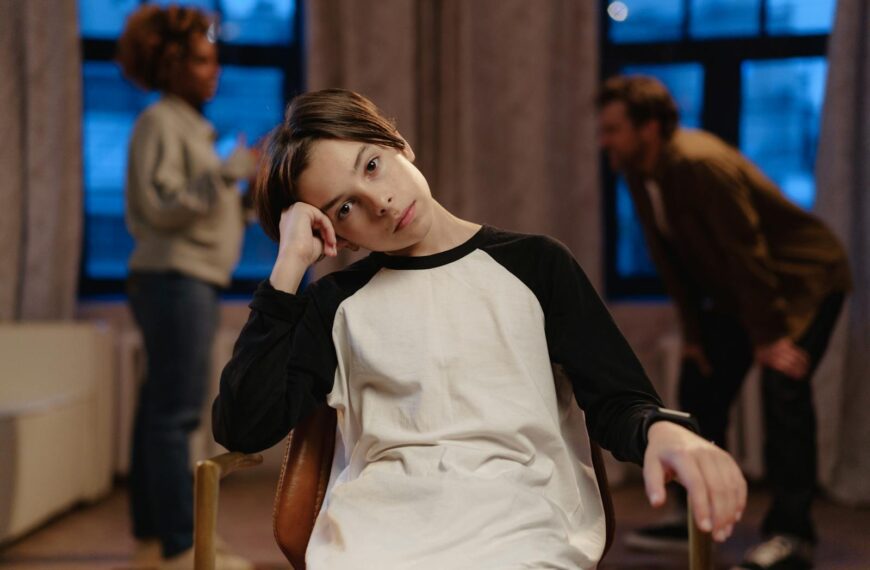 A young boy in a black and white shirt looks sad as his parents argue in the background.