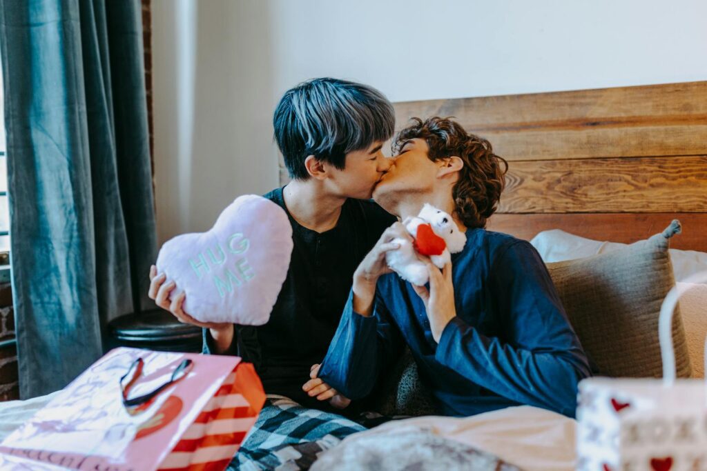 A loving couple sharing a kiss and exchanging gifts in a cozy bedroom setting.