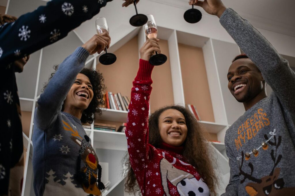 Group of friends in festive sweaters cheering with champagne indoors.