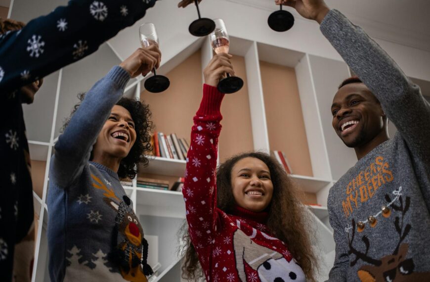 Group of friends in festive sweaters cheering with champagne indoors.