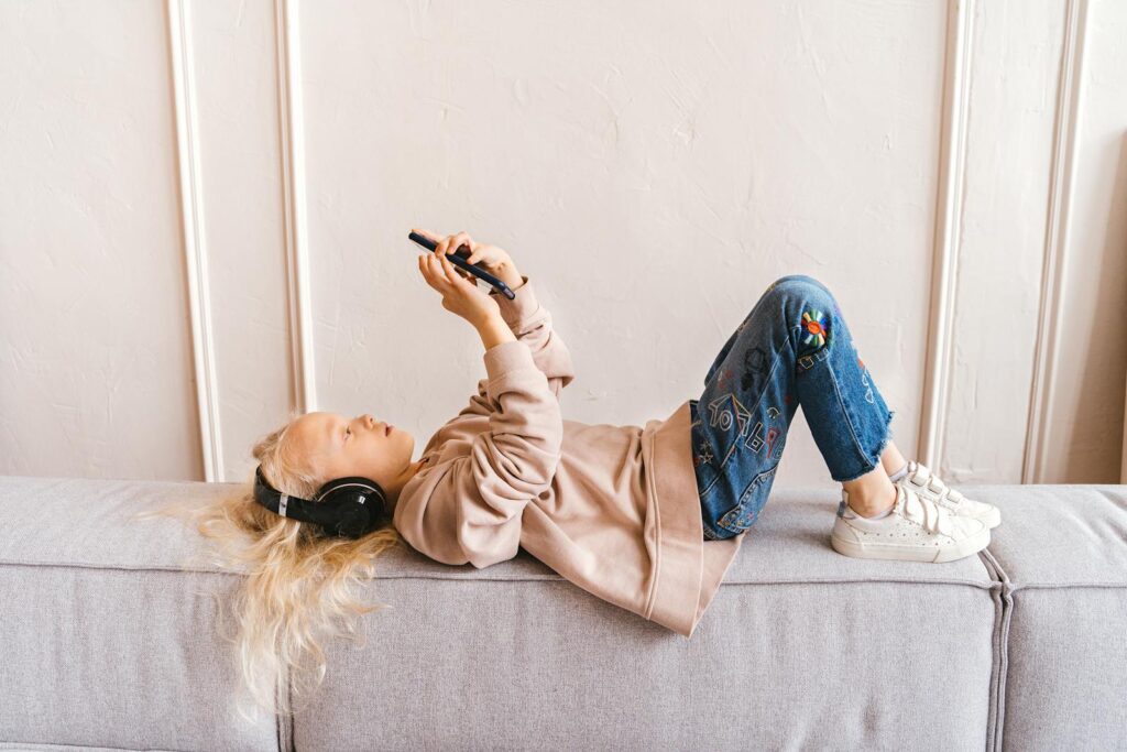 Young girl enjoying leisure time on sofa with headphones and smartphone indoors.
