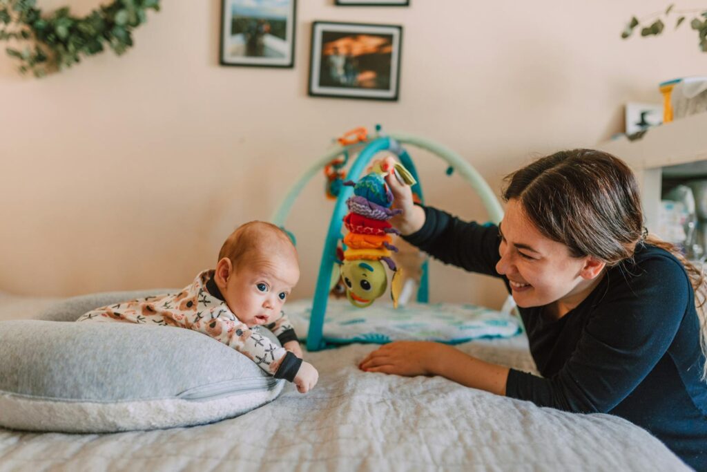 A joyful mother playing with her baby on the bed in a warm, cozy bedroom setting.