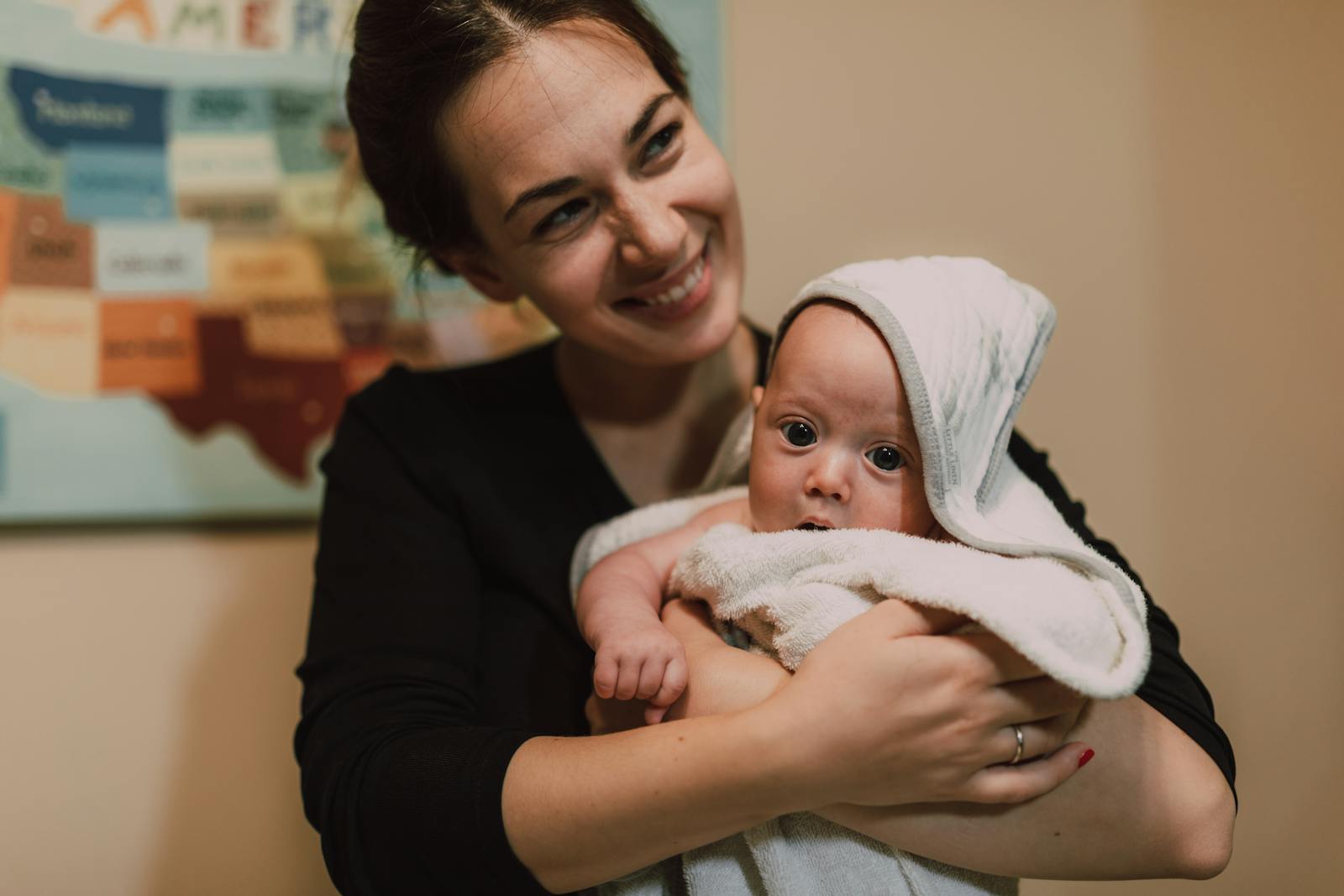 A joyful mother holding her cute infant wrapped in a towel indoors with a focus on warmth and affection.