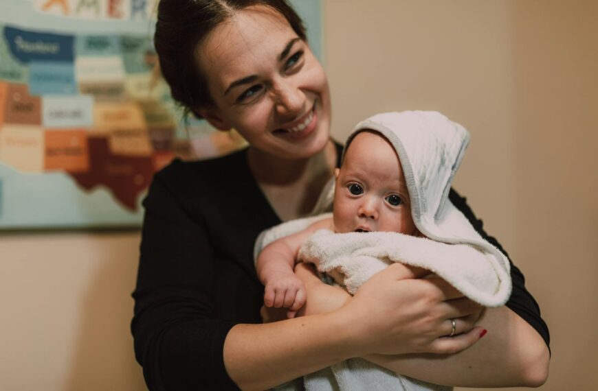 A joyful mother holding her cute infant wrapped in a towel indoors with a focus on warmth and affection.