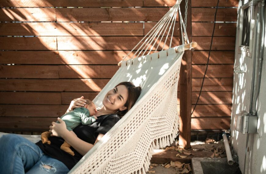 Mother smiling holding baby in a hammock outdoors enjoying a sunny day.