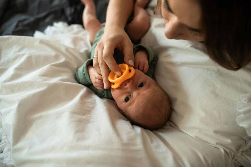 A tender moment of a mother with her newborn baby holding a pacifier indoors.