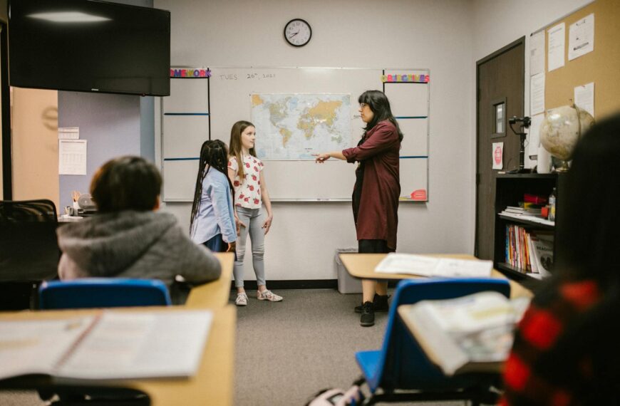A teacher instructs students in a classroom with a world map and educational materials.
