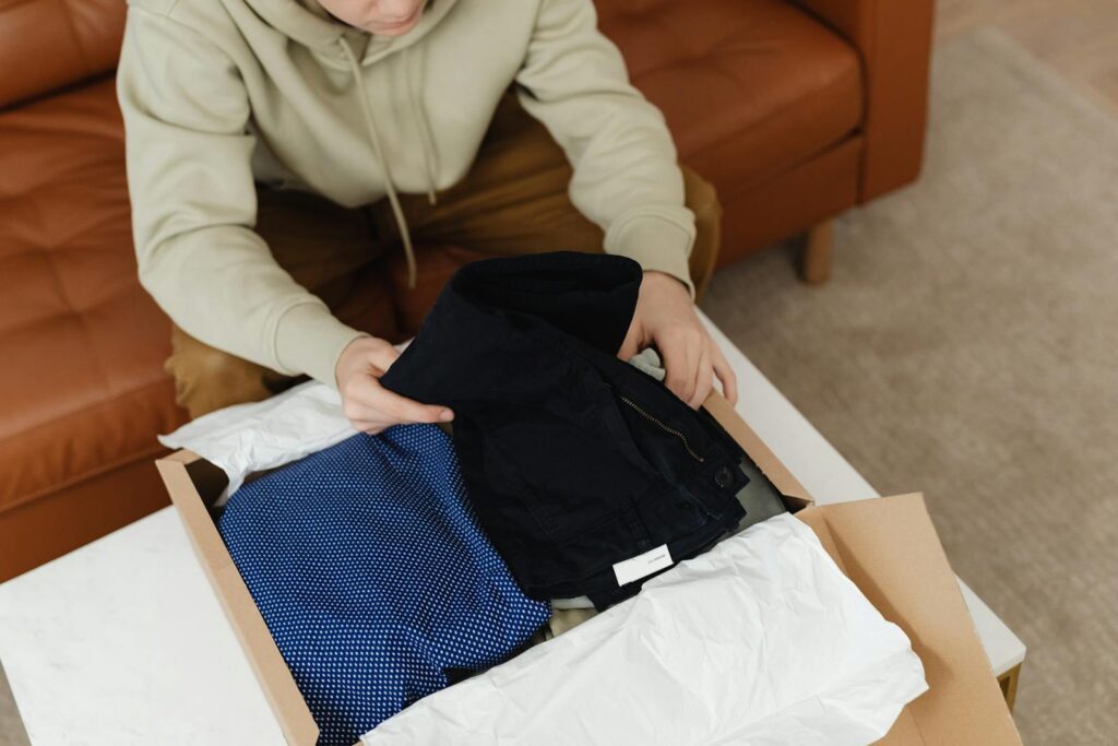 Person unboxing clothes from a cardboard box on a white table inside a living room.