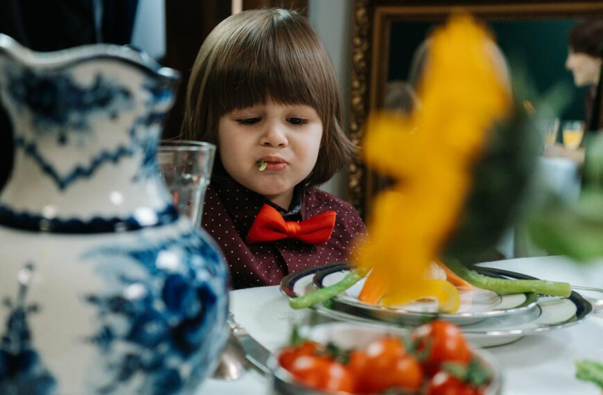 A young child with a humorous expression while eating vegetables at a dining table.