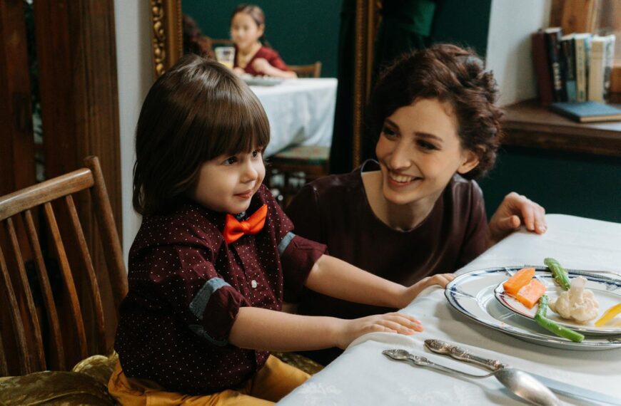 A mother and her son smiling during a meal in a fine dining setting, with healthy foods on the table.