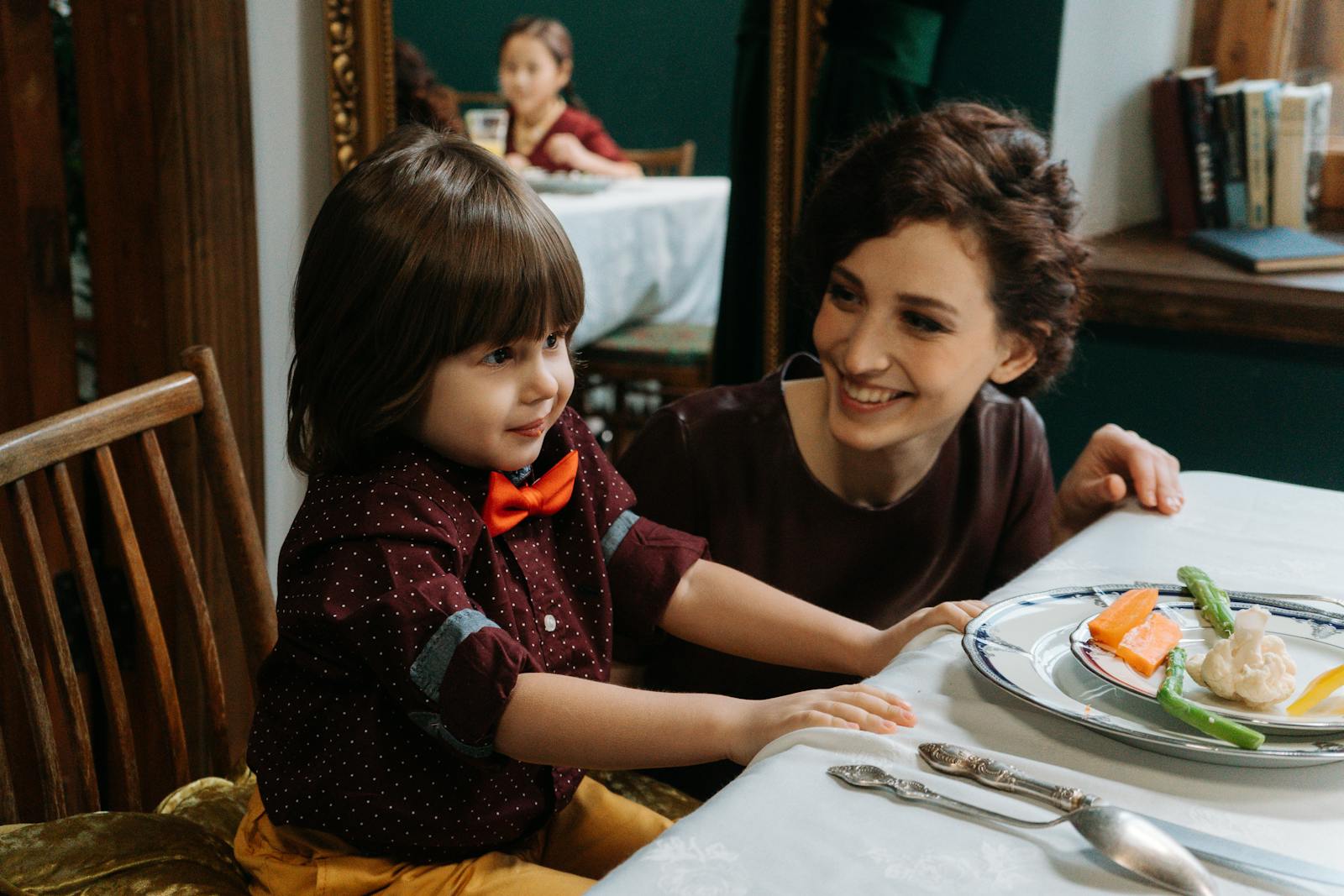 A mother and her son smiling during a meal in a fine dining setting, with healthy foods on the table.