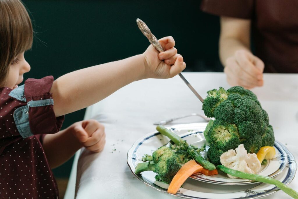 A child enthusiastically eating a plate full of fresh vegetables at the dining table.