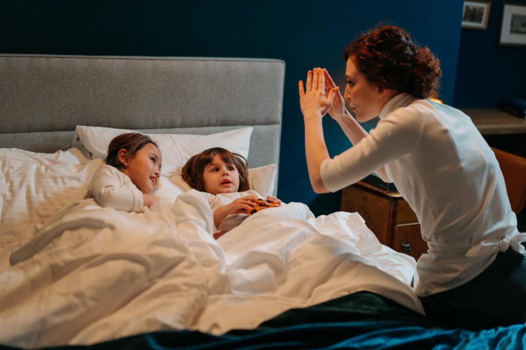 A caregiver tells a comforting bedtime story to two children tucked in bed for a peaceful evening.