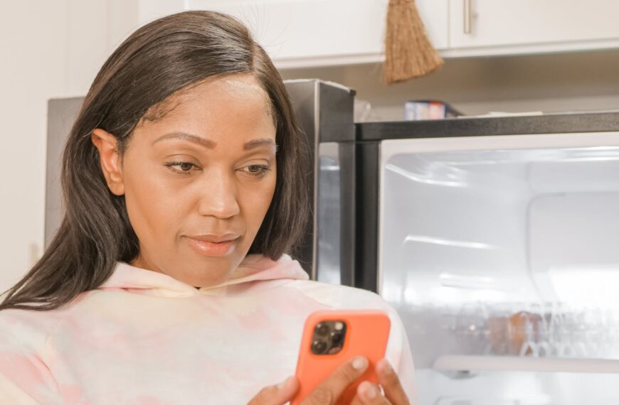 African American woman focused on her smartphone in a cozy kitchen.