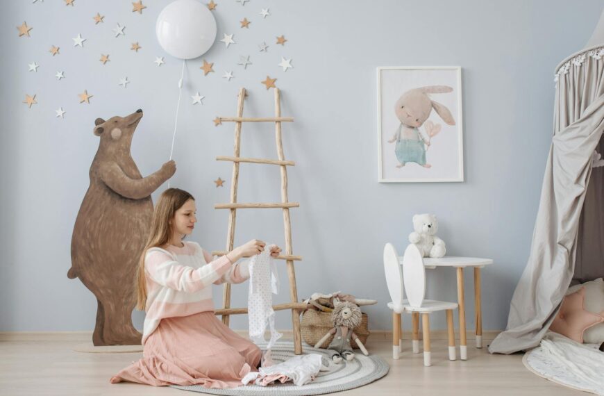 A woman folds baby clothes in a beautifully decorated nursery with a bear and star-themed design.