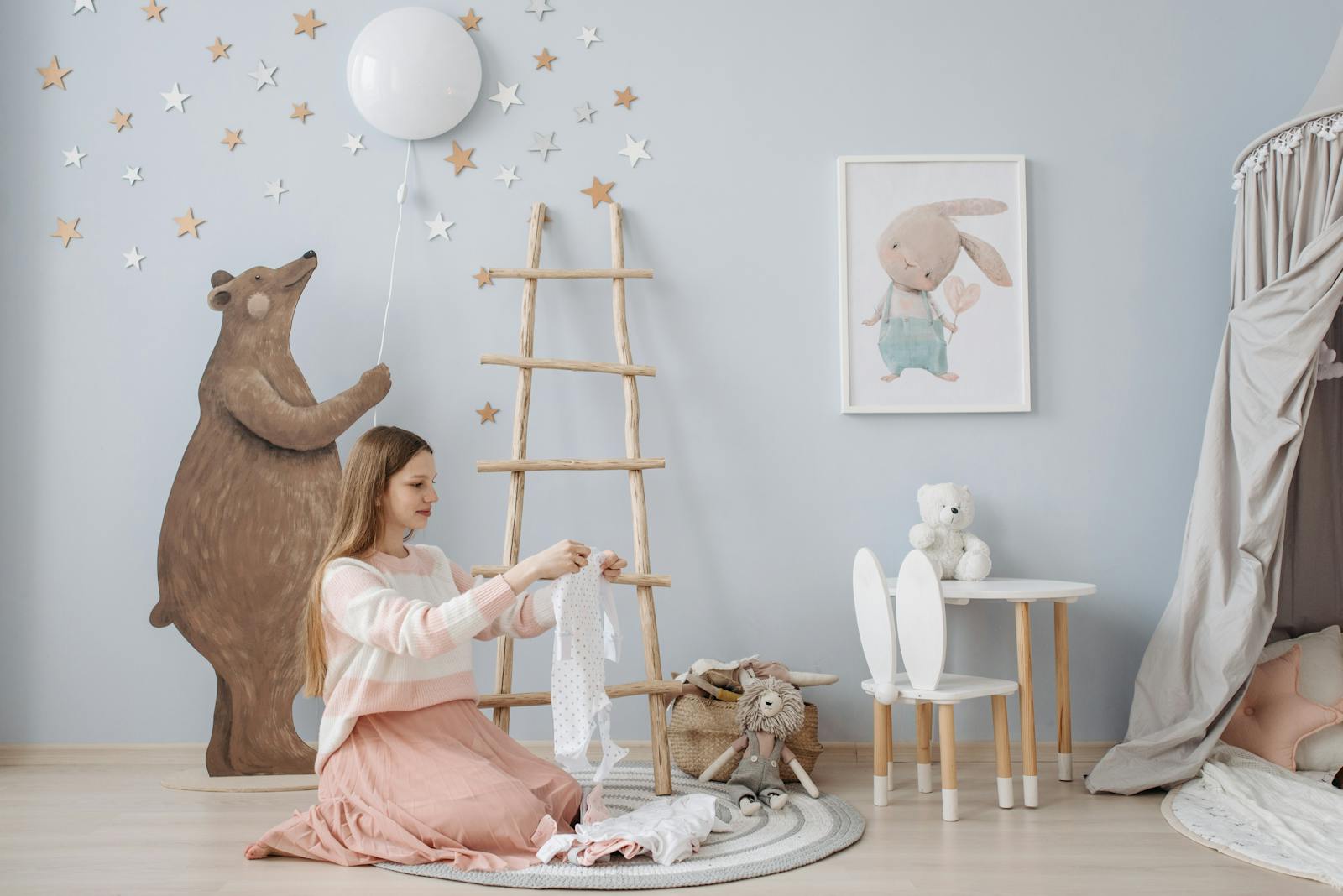 A woman folds baby clothes in a beautifully decorated nursery with a bear and star-themed design.