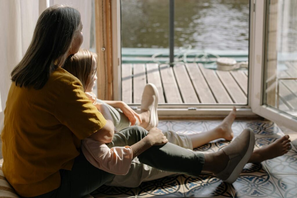 Heartwarming moment of a grandmother and granddaughter sitting by the lake, enjoying a peaceful day.