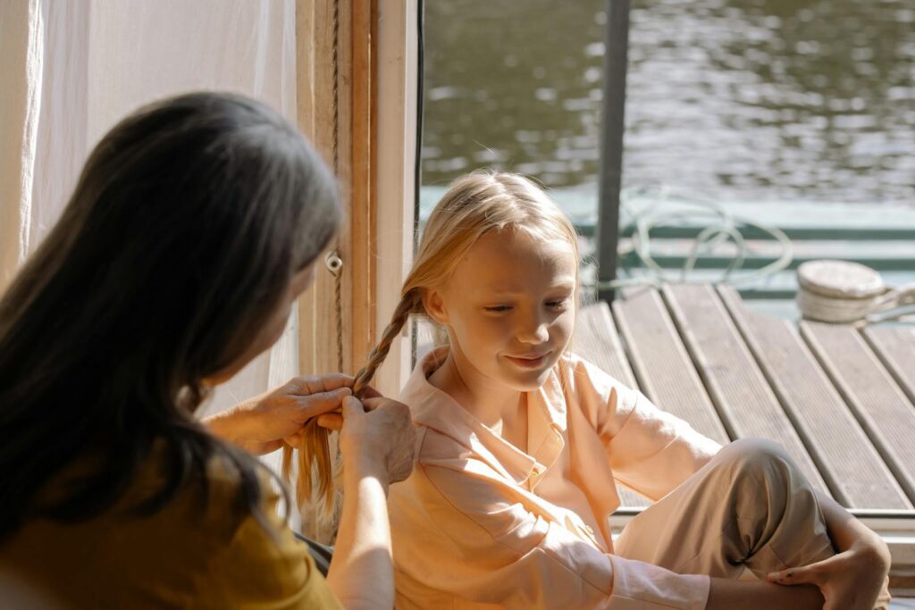 A serene moment of a grandmother braiding her granddaughter’s hair by the lakeside.