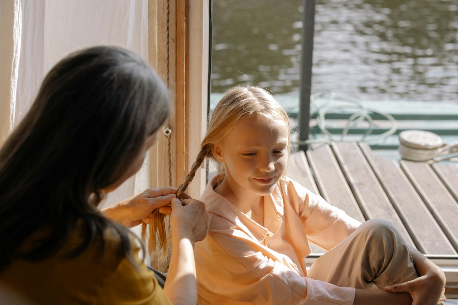 A serene moment of a grandmother braiding her granddaughter’s hair by the lakeside.