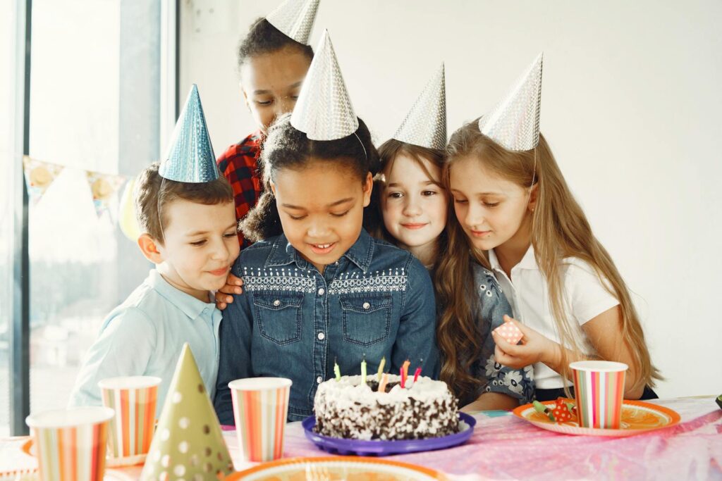 Children gathered around a birthday cake with party hats, celebrating joyfully together.