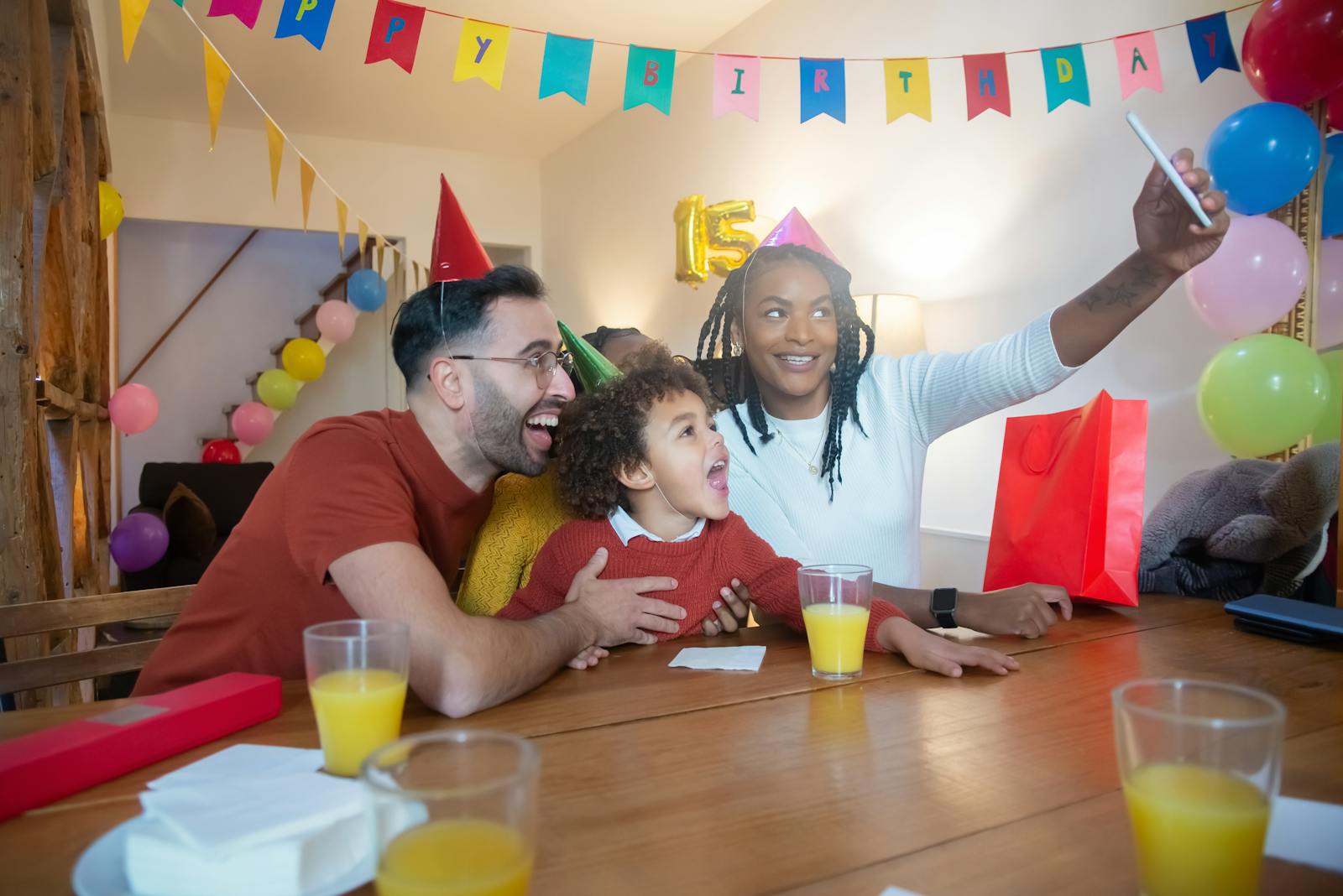 Happy family celebrating a child's birthday with balloons and party hats, capturing a joyful moment with a selfie.