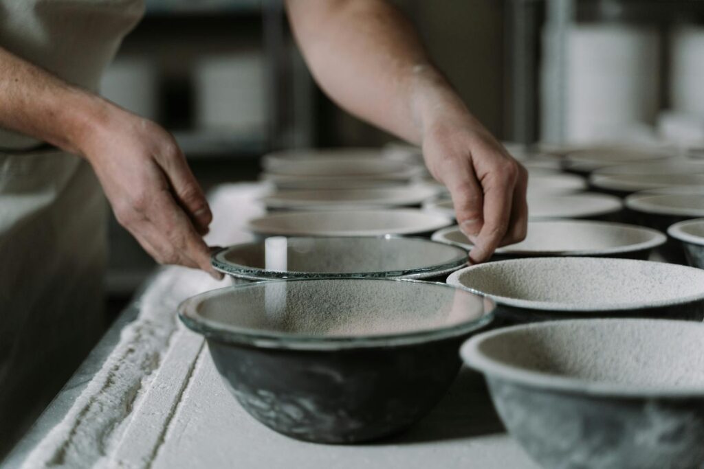 Hands crafting pottery bowls in a studio, showcasing artisanal manufacture and attention to detail.