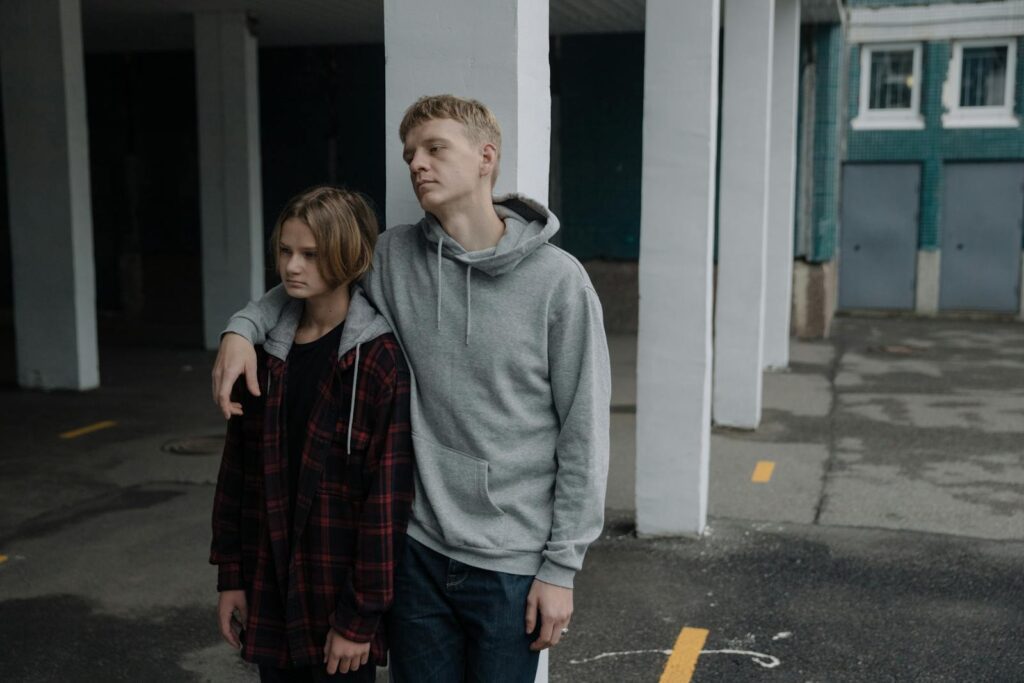 A brother and sister in hoodies stand together outside, embracing a casual urban lifestyle.