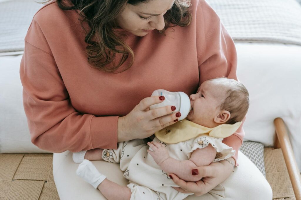 A mother lovingly feeds her baby with a bottle, relaxing in a cozy room setting.