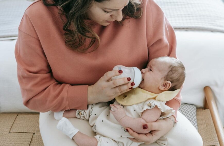 A mother lovingly feeds her baby with a bottle, relaxing in a cozy room setting.